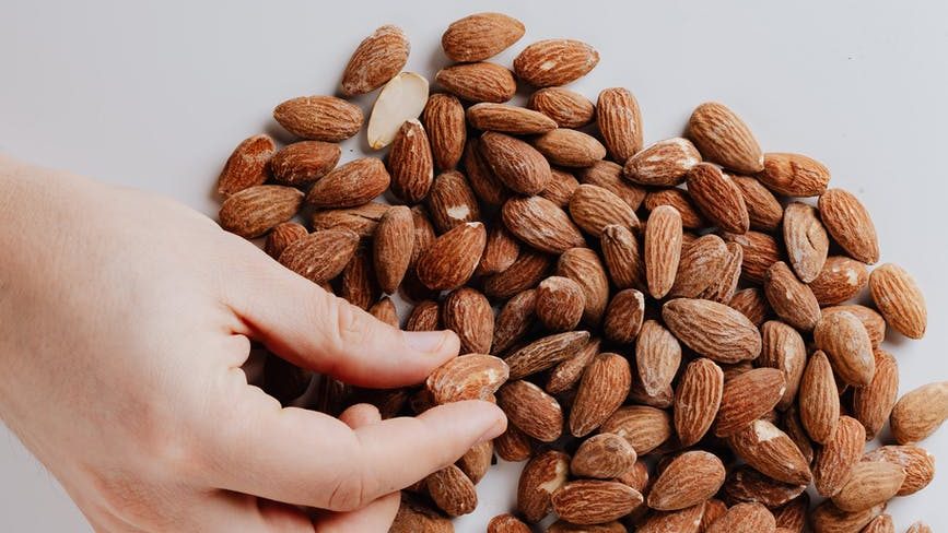 crop person taking almond nut from white table