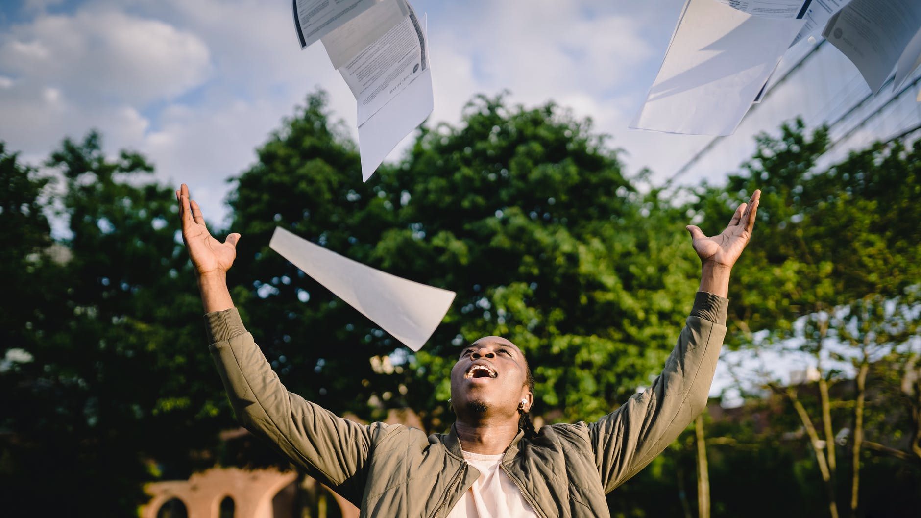 happy student throwing papers in air in park