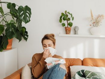 woman sitting on sofa and blowing her nose into a tissue