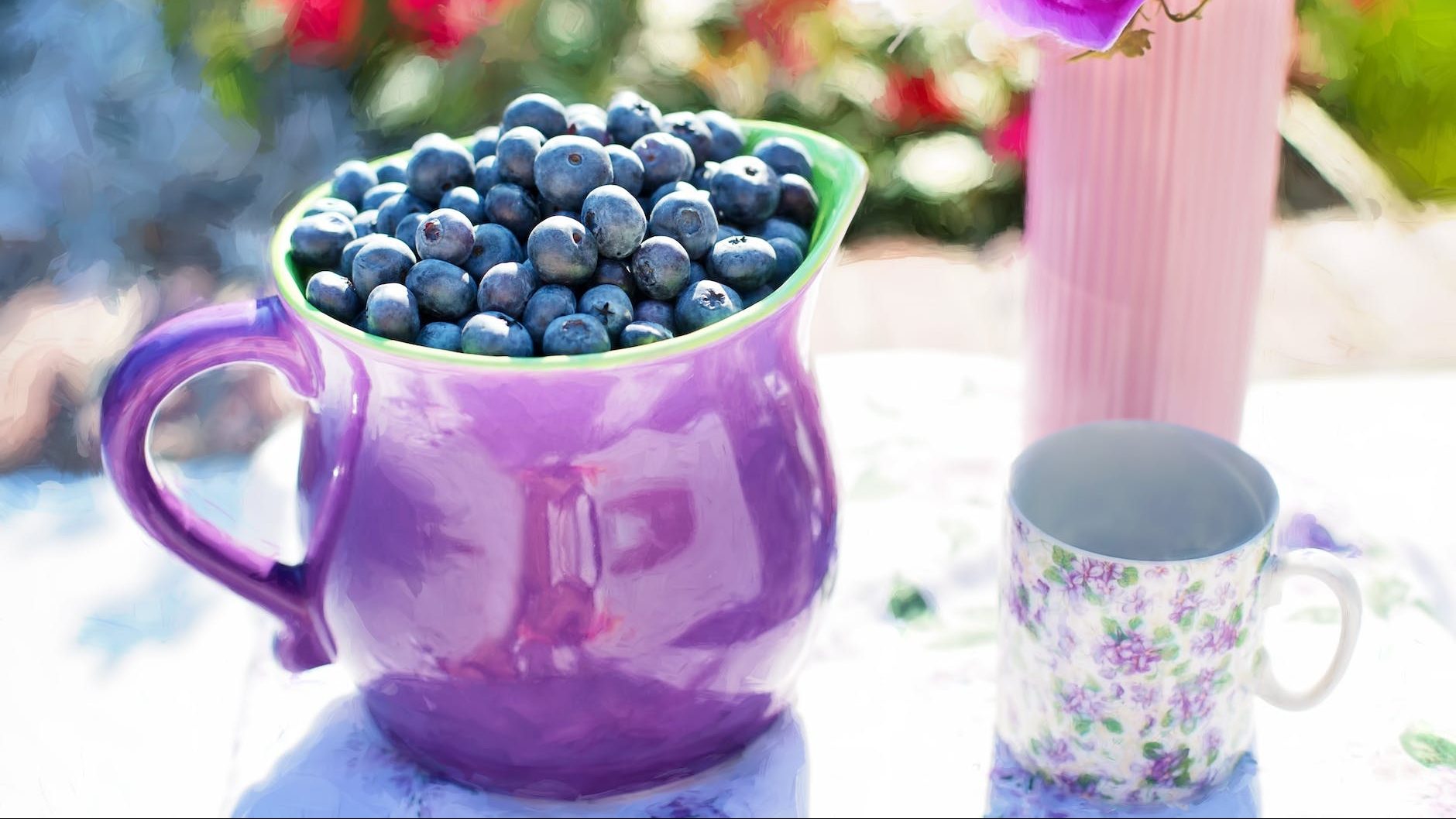 black berries on purple container beside white and purple floral mug