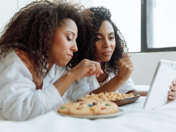 two women with curly hairs watching on a digital tablet with snacks