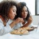 two women with curly hairs watching on a digital tablet with snacks